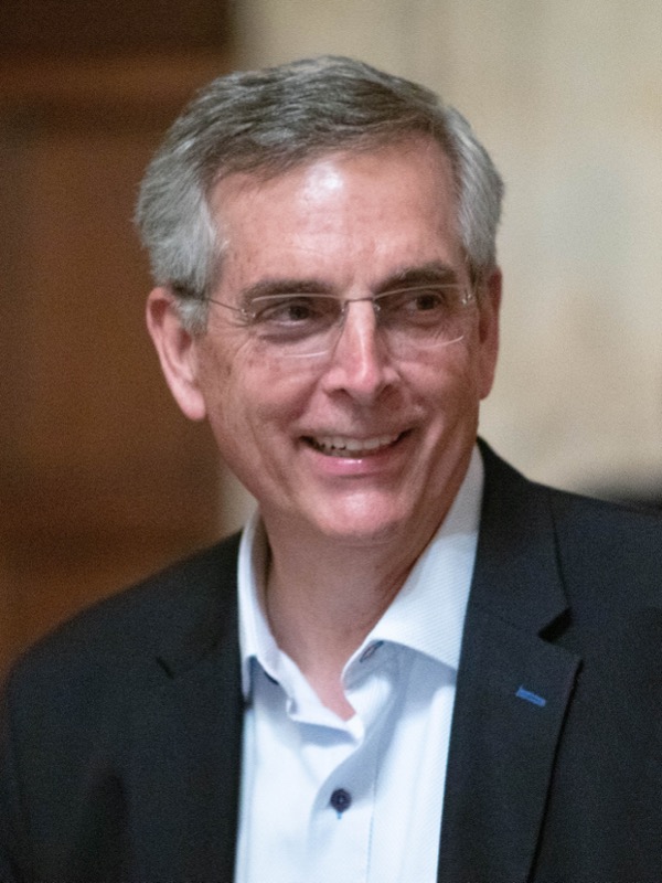 Brad Raffensperger, Georgia Secretary of State, in a 2022 portrait. He wears a dark blazer over a light blue shirt, with gray hair and glasses.