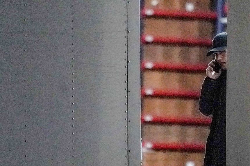 Tulsi Gabbard speaks on her phone while partially visible behind a truck door. Behind her, rows of sealed ballot storage boxes with red tape are stacked inside the truck.