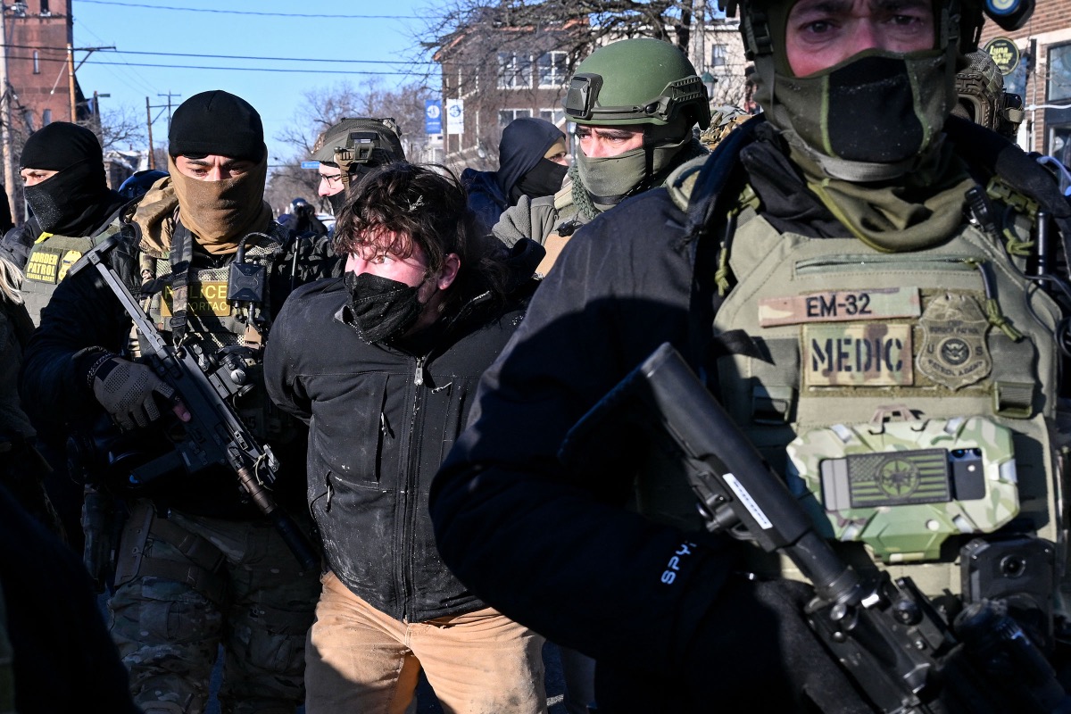 A federal agent in riot gear tying yellow police tape near the scene of the shooting in Minneapolis