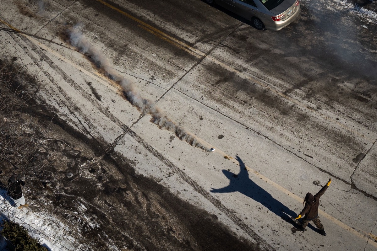 A protester sitting cross-legged with hands raised in front of agents in riot gear
