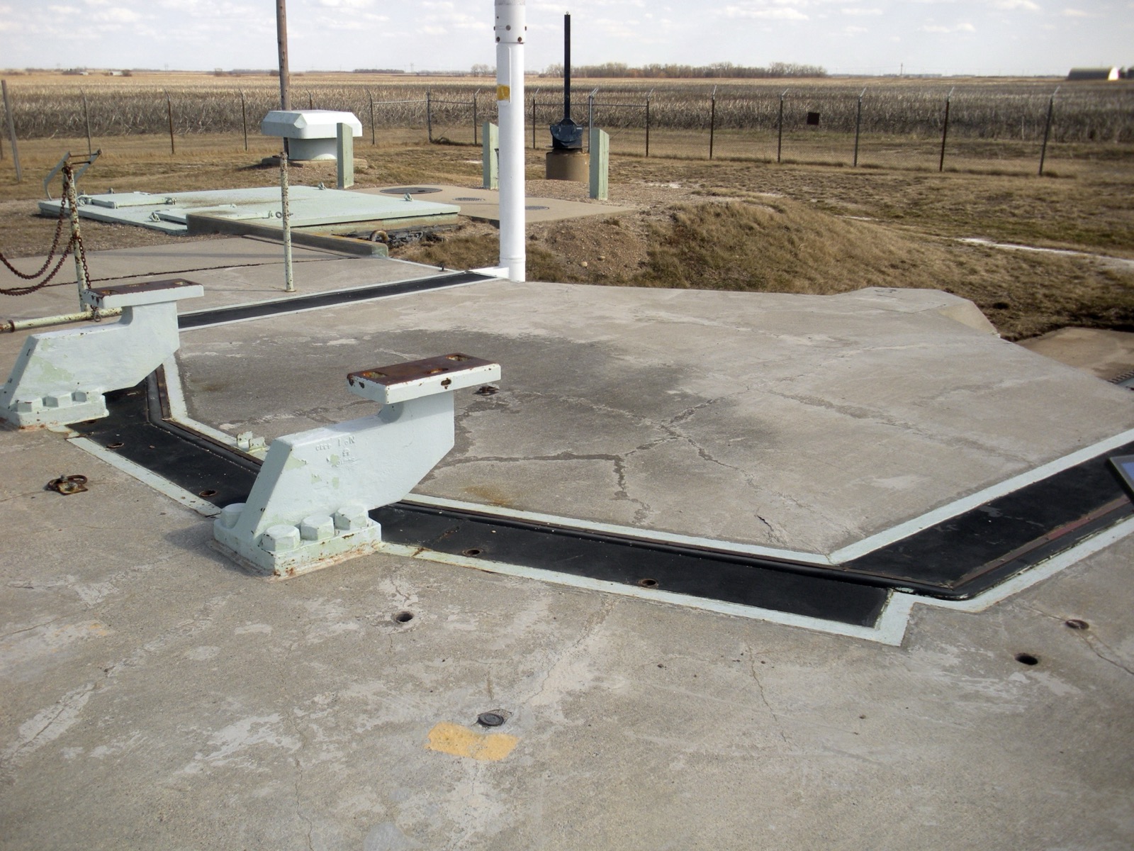 The massive concrete launcher door of a Minuteman missile silo, surrounded by prairie grass and security fencing under an open sky